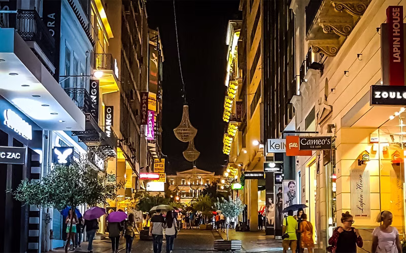 Winkelstraat in Athene bij avond met verlichte etalages en wandelend publiek