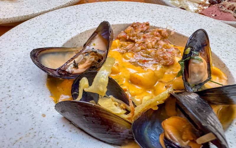 Gerecht met mosselen, pasta en krokante topping op een diep bord