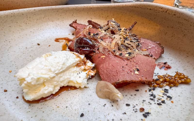 Gerecht met pastrami, romige kaas en zoetzure kersen op een stenen bord