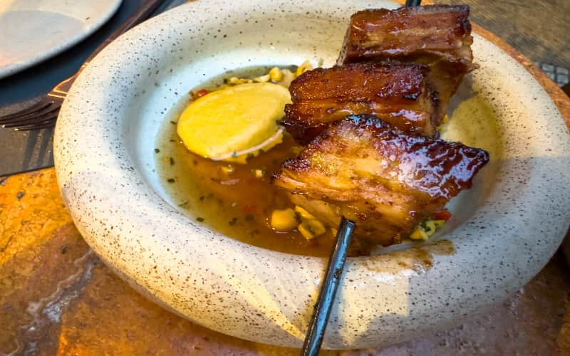 Gelakt buikspek met saus en mais in een stenen kom