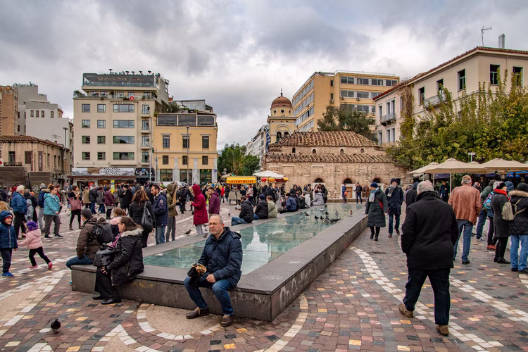 Het Monastirákiplein met de fontein, wandelende bezoekers en de moskee op de achtergrond