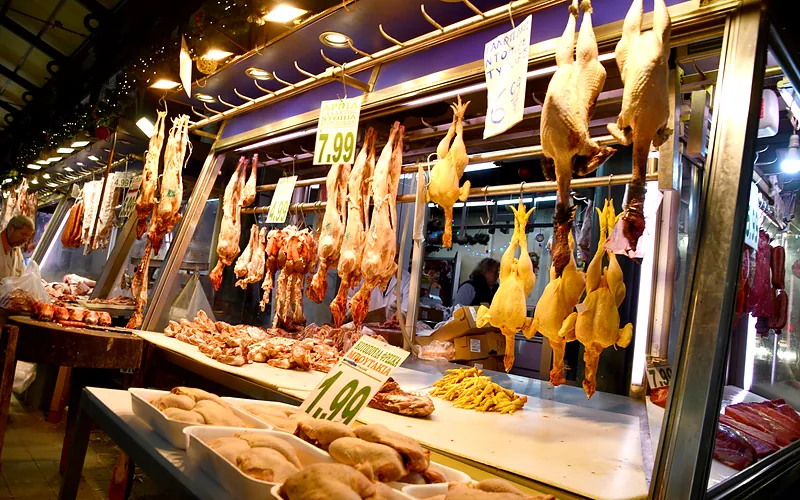 Een vleeskraam in de Varvakios-markt met opgehangen kippen en vlees achter glas, met prijsbordjes van 7,99 en 1,90 euro