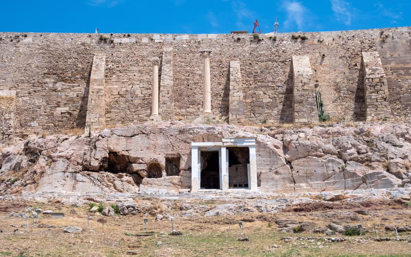 De rotswand boven het Dionysustheater met een ingemetselde ingang in de grot en de vestingmuur van de Akropolis erboven