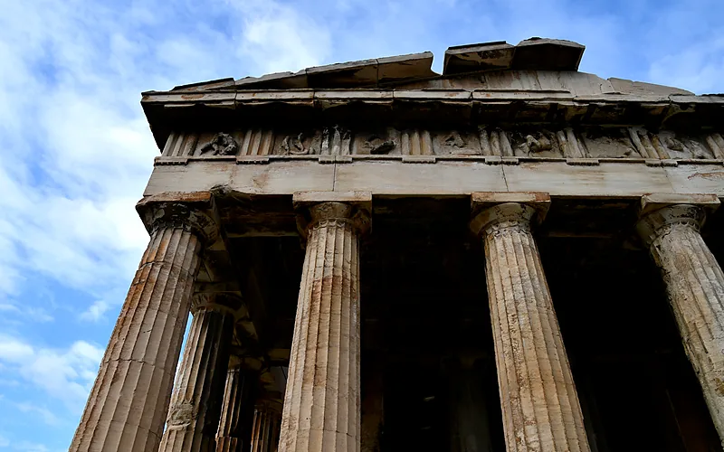 De zuilen en de fries van de Tempel van Hephaistos van onderaf gezien tegen een wolkenlucht