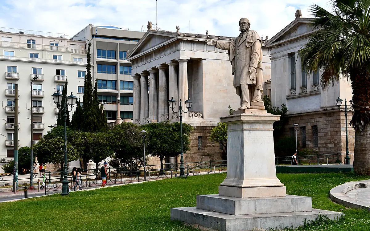 Een marmeren standbeeld van een man op een hoge sokkel voor het gebouw van de Nationale Bibliotheek in Athene